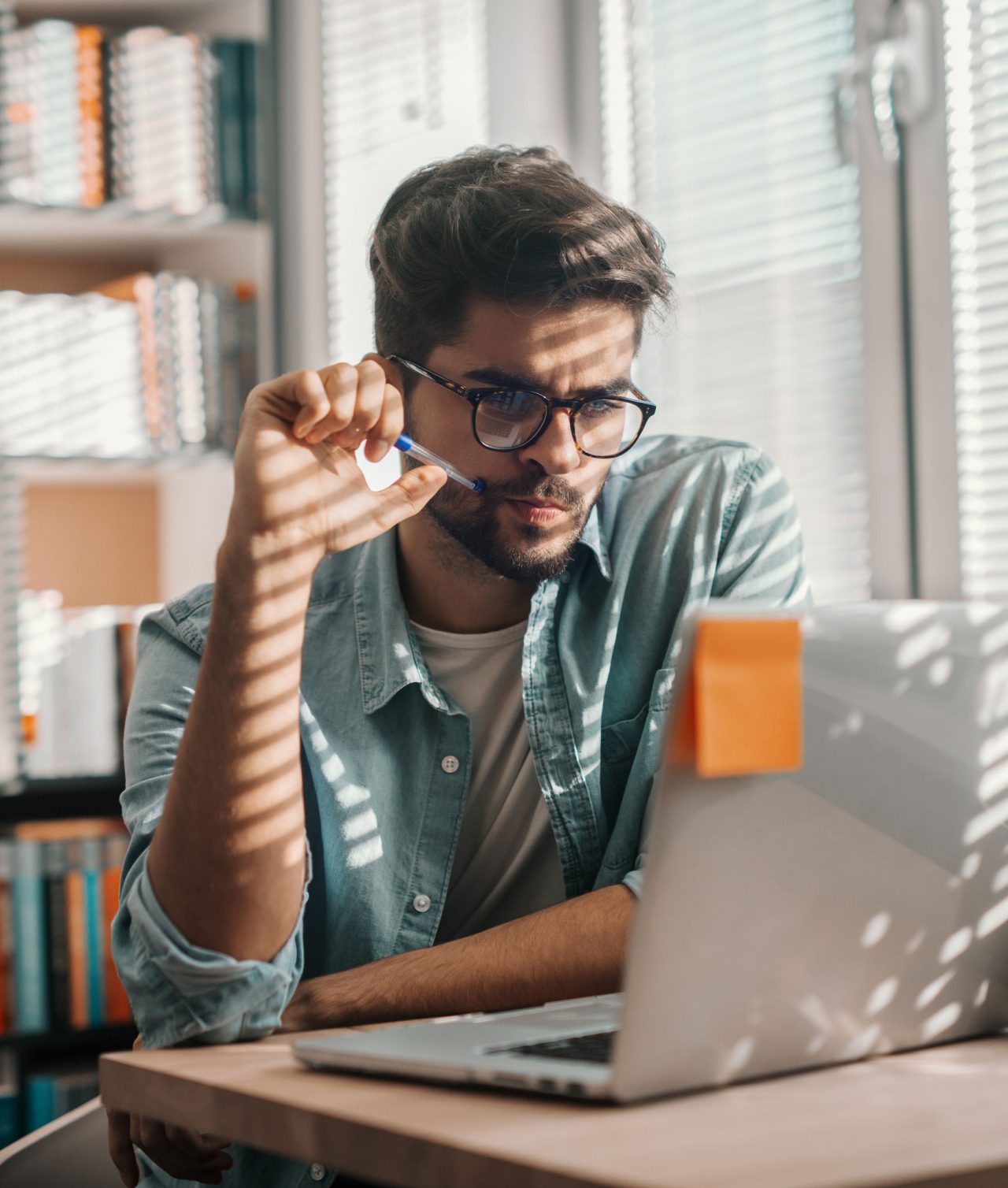 Chico consultando un documento mientras trabaja con un ordenador portátil